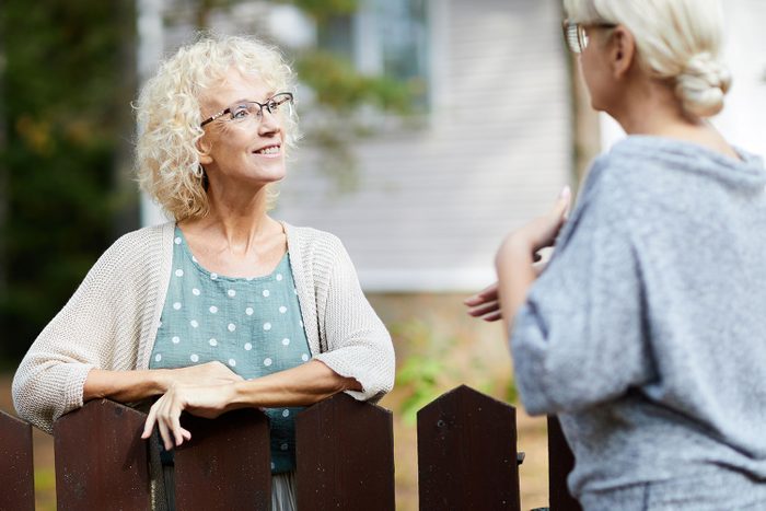 Two mature female neighbours talking through fence about everyday life stuff