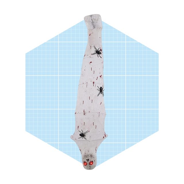 A creepy, elongated figure draped in a white cloth features red eyes and black spider decorations, set against a light blue grid background.