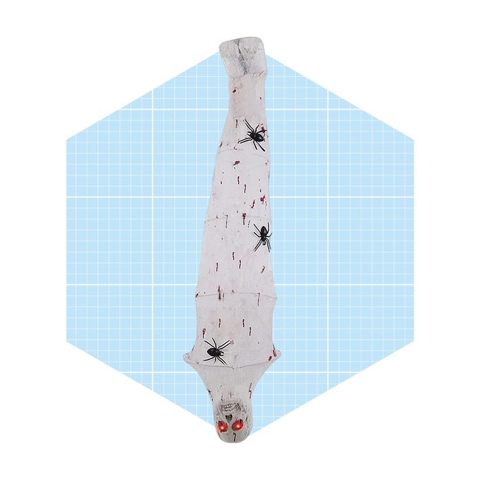 A creepy, elongated figure draped in a white cloth features red eyes and black spider decorations, set against a light blue grid background.