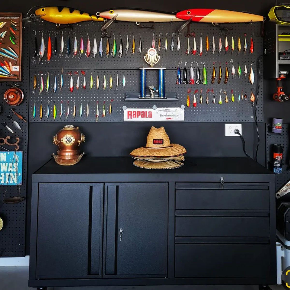 A black cabinet displays fishing lures hanging on a pegboard. Fishing trophies and equipment are nearby, amidst a well-organized garage environment.