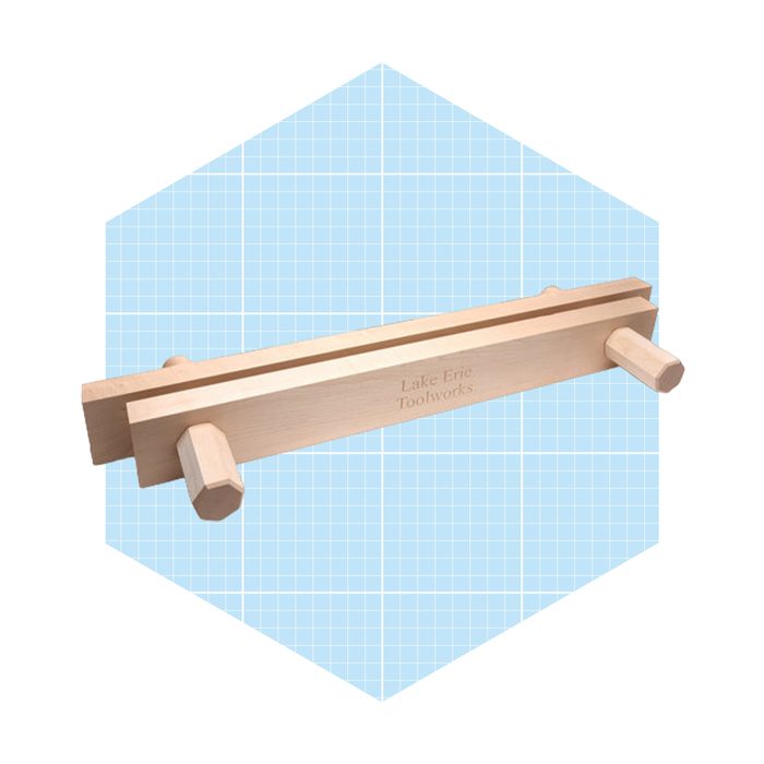 A wooden tool with two handles rests on a blue grid background, designed for woodworking tasks, showcasing an engraved brand name.