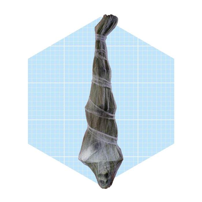 A large, wrapped object stands upright against a light blue geometric background, suggesting a cocoon-like shape with a tapered top and broader base.