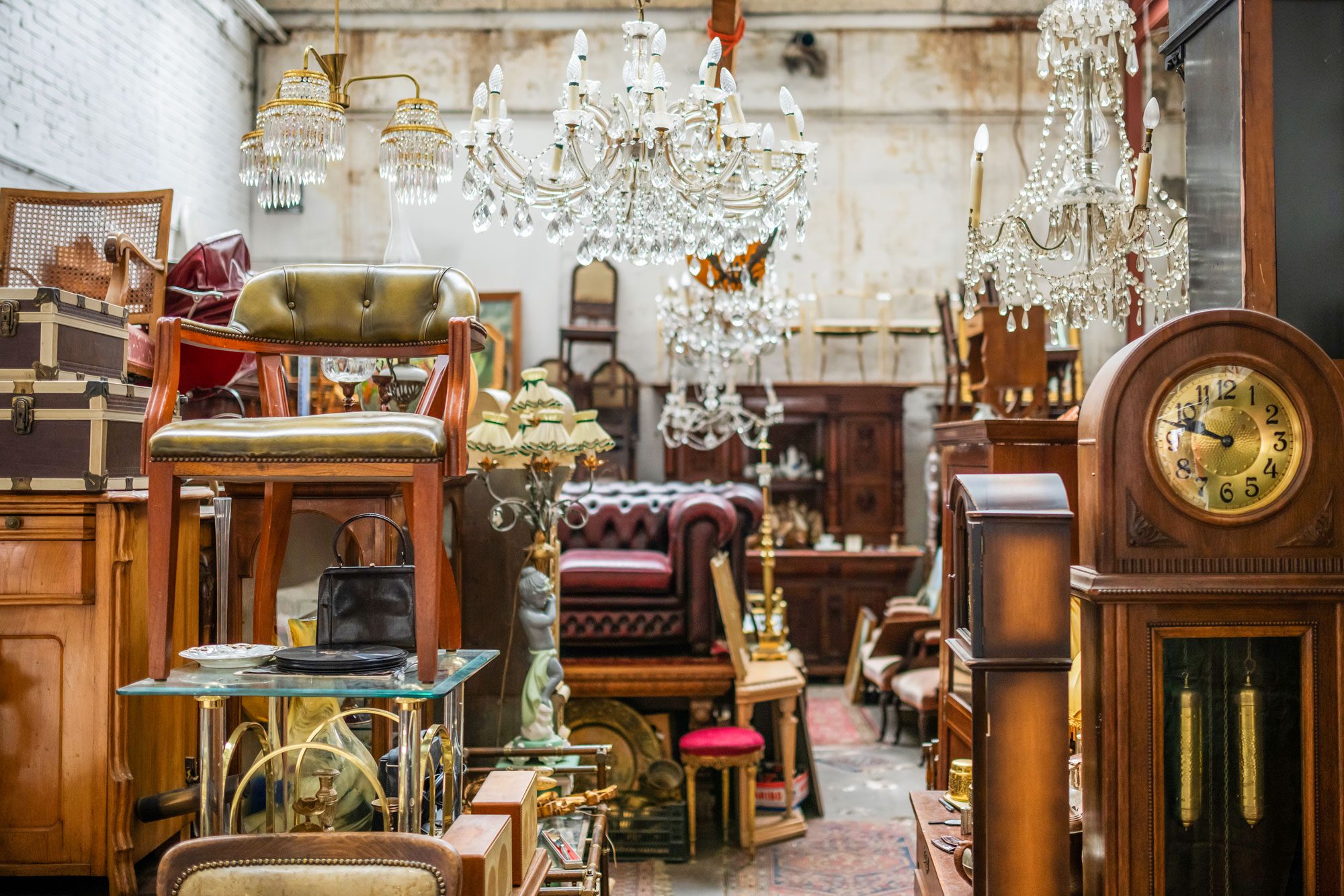 Various antique furniture pieces and decor items occupy a cluttered space, showcasing a mix of styles and materials under soft lighting.