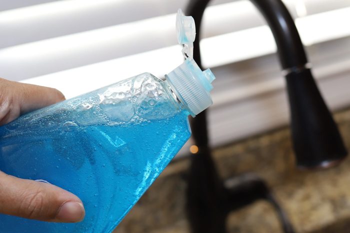 A woman holding a bottle of dish detergent in her hand