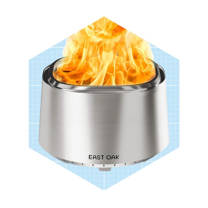 A stainless steel fire pit emits vibrant flames, surrounded by a light blue grid background, suggesting an outdoor or cozy environment. Text reads 