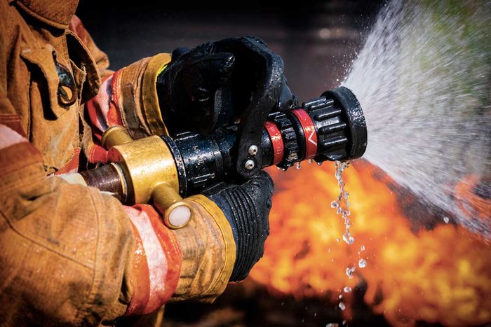Close up of Firefighters Hand Holding Fire Hose Extinguishing House Fire.