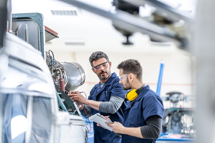 Young aviation mechanics studying to repair engine medium shot