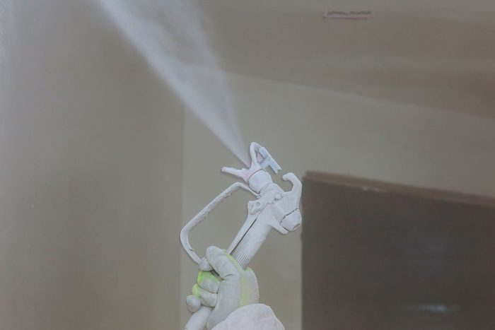 House Painter Spray Painting Worker Painting Wall With Spray Gun In White Color