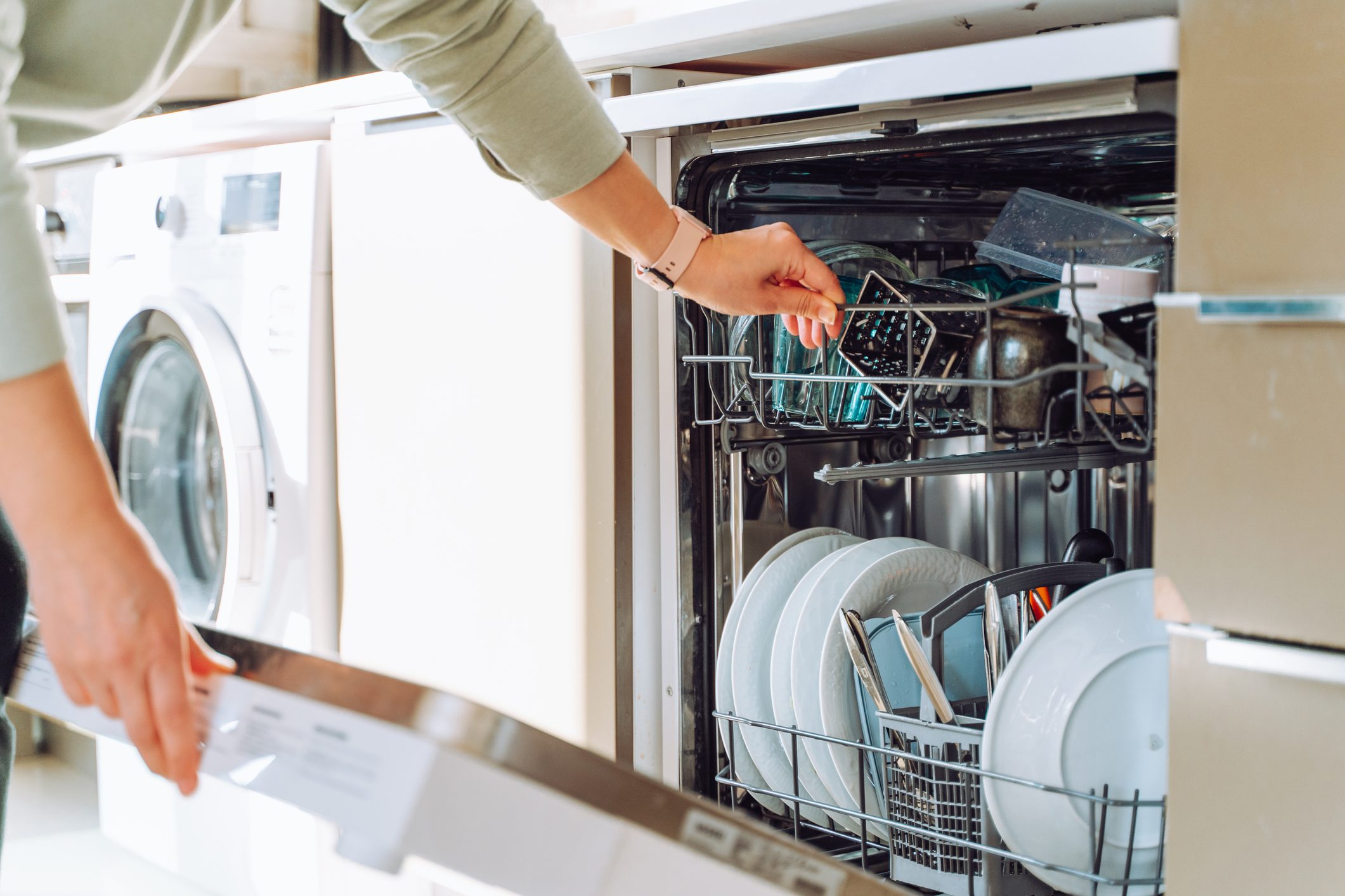 Close up cropped hands loading dish washing machine near washing machine in modern built in kitchen