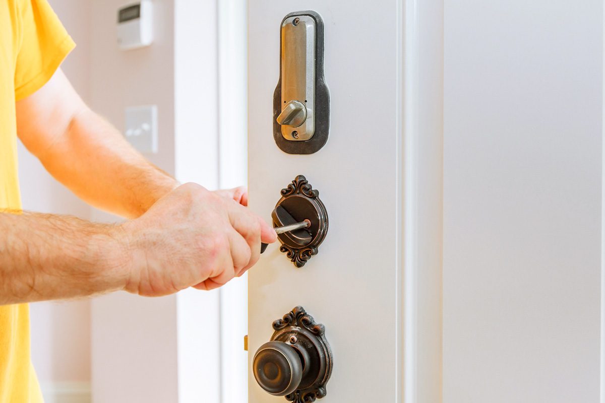 Closeup of a professional locksmith installing or repairing a new deadbolt lock on a house door with the inside internal parts of the lock visible.